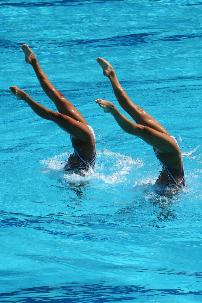 Deux athlètes exécutant une figure synchronisée en natation artistique, les jambes hors de l’eau et parfaitement alignées.